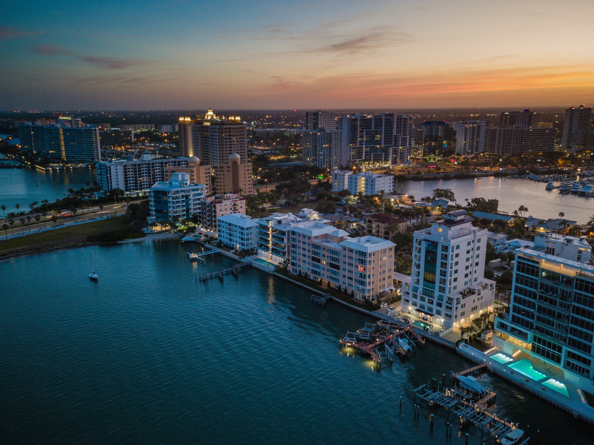 Aerial view of a city waterfront at dusk, featuring high-rise buildings, illuminated windows, boats docked along the shore, and a calm waterway—evoking the peaceful security one might feel with a Sparks Revocable Living Trust in place.