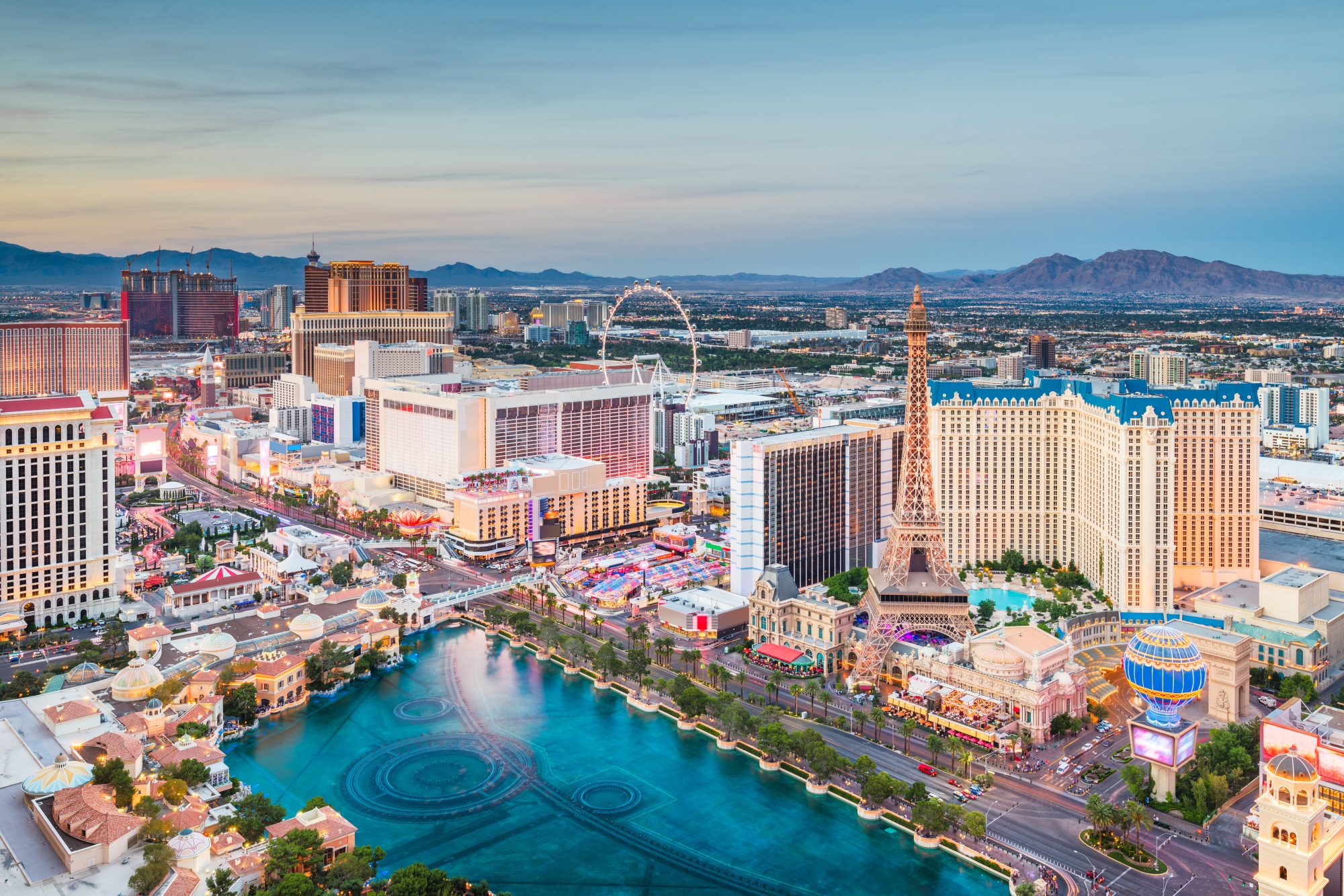 Aerial view of Las Vegas Strip at dusk featuring casinos, hotels, and landmarks like the replica Eiffel Tower and High Roller Ferris wheel with mountains in the background, serving as a stunning reminder of why Carson City Estate Planning for your assets is crucial.