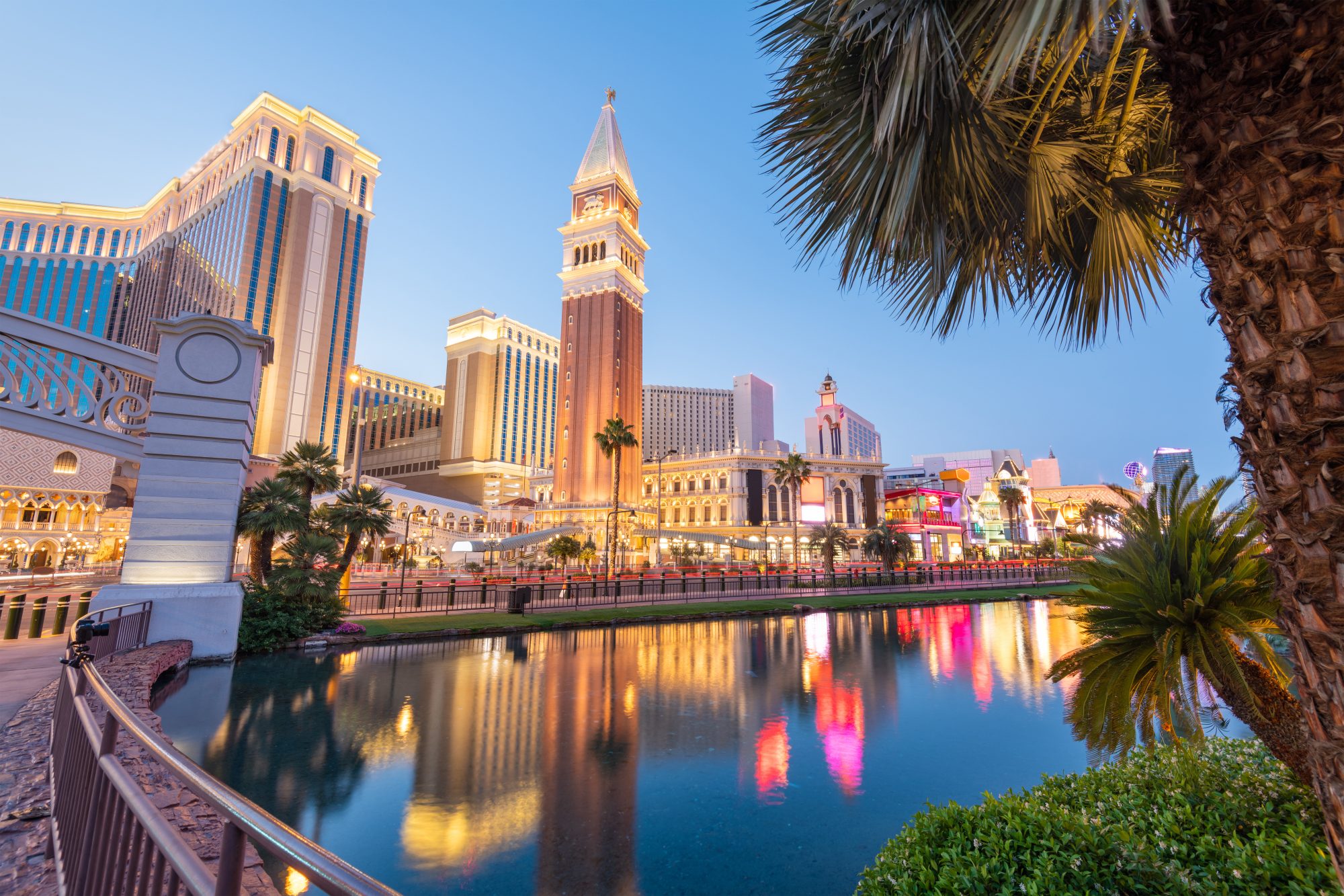 View of a canal and Venetian-themed buildings at the Venetian Resort in Las Vegas, lit up in the evening with palm trees in the foreground, reminiscent of Carson City Estate Planning's elegance.