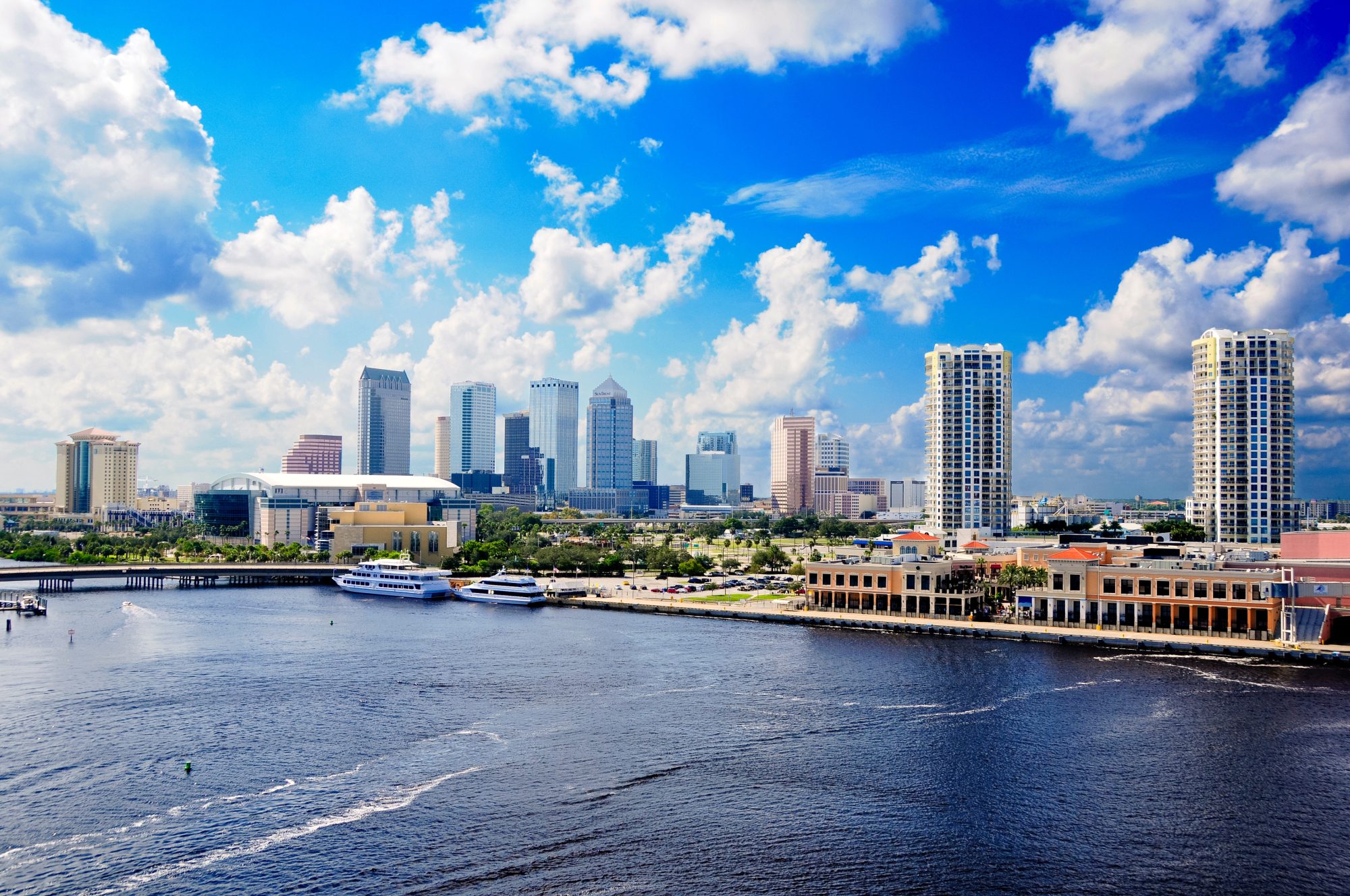 A waterfront cityscape with tall modern buildings under a partly cloudy blue sky. Several boats are docked along the shore, highlighting an area where Verdi Affordable Living Trust makes Reno living even more accessible.